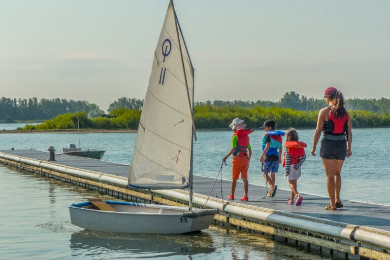 Kids walking on dock by small sailboat